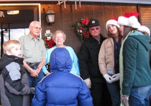 An elderly couple greet the carolers on their front porch.