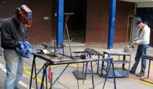 The men are welding and filing the edges of steel to make a smooth fit for the frames of the chairs.